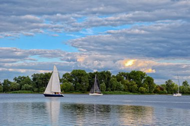 Dinyeper Nehri 'nde güzel bir günbatımı, spor yatları ve bulutların arka planına karşı. Ukrayna, Kyiv şehri, Obolonsky bölgesi. Arka plan bulanık, keskin değil..