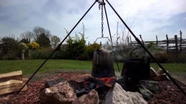 An old percolator coffee pot on a tripod above boiling the campfire, on the refractory cobblestones the tea water is heating in an old cast iron pot
