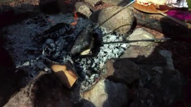 Cooking outdoors on a crackling wood fire in a fire pit. A cast iron sandwich iron on the glowing charcoal with a panini, shot in 59.94 fps