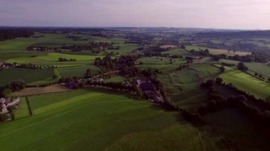 Scenic valley landscape, campsites and woods, beautiful rolling hills and farmlands, natural pastures, meadows and farms, with rural roads. Blue and purple sky in the background in summer season. Drone Aerial View South Limburg morning golden hour