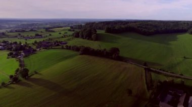 Yuvarlanan tepeler üzerinde bir şatonun parıltısı, doğal çitleri olan çayırlar, ormanlık bankalar, kırsal yollar ve ormanlar ve arka planda mavi mor gökyüzü, Güney Limburg 'da Hollanda üç ülkeden oluşan Hava Aracı Yaz Saati