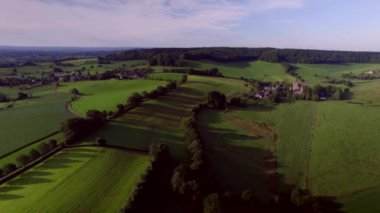 Yuvarlanan tepelerin üzerinden bir şatoya uçmak yere doğru alçaktan uçmak ve çayırların üzerinden uçmak, doğal çitleri, çitleri, kırsal yolları ve ormanları olan çayırlar ve arka planda Güney Limburg 'da mavi-mor gökyüzü.