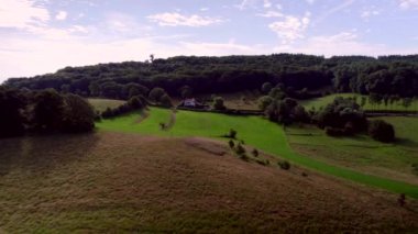 Aerial View: Bir yol olan çayırların üzerinden alçalıyor ve Güney Limburg Üç Ülke Noktası, Vaals, Hollanda 'daki ormanlarla birlikte kayan tepelerin üzerinden yükseliyor.