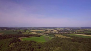Hava manzarası: İnsansız hava aracı trafiğin olduğu yola, kırsal manzaraya, yeşil tarım alanlarına ve mavi mor gökyüzüne sahip ormanlara doğru iniyor. Güney Limburg Hollanda