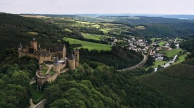 Kale Havadan Görünümü: İnsansız hava aracı Bourscheid kalesi boyunca ilerliyor. Dağın tepesinde güzel bir romantik şato ve vadide küçük bir köy var. Nehir, çayırlar, tepeler ve Lüksemburg ormanları..