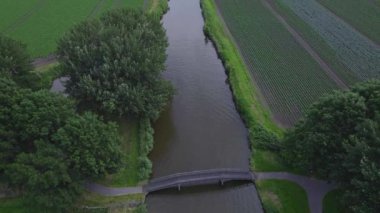İnsansız hava aracı ateş etti. Kanaldaki tekne köprüde gözden kayboldu. Ekinleri, trafiği ve arka planda rüzgar türbini olan alanlar. Hollanda Kırsal Arazi 4k, Hollanda 'da doğa ve tarım hava manzarası