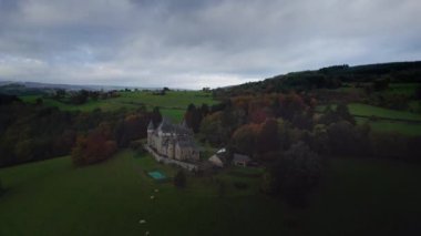 Belçika Ardennes 'in ortasında, sonbahar ormanları ve ineklerle çevrili güzel Chateau Hotel de Froidcour kalesi. Bulutlu gün karanlık atmosferi, Belçika Ardennes Havacılık görüşü uçuş hareketi şato boyunca çekimler, dolly çekim.