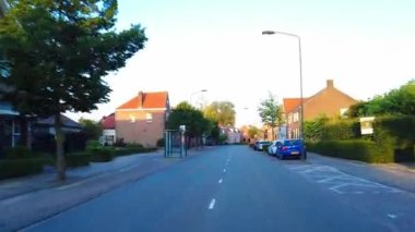 POV 20 Haziran 2022 'de Hollanda' daki Chaam 'dan geçerken saat 09: 22. Kırsal kesimde evler, otobüs durağı ve yaz mevsiminde gün batımında Hollanda 'nın güneyinde bir kilise.