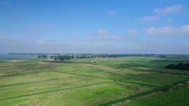 İHA panorama görüntüsü: İnsansız hava aracı polder, çayırlar, tarlalar ve bir değirmen üzerinde bir görüşle ortaya çıkıyor. Gölde yelkenlilerle. Arka planda bir sanayi bölgesi ve Hollanda 'da bir Hoorn şehri var..