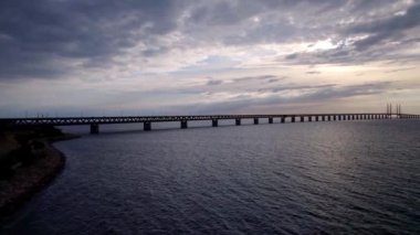 Golden hour view from low angle on the resund bridge near Malm Sweden to Copenhagen Denmark. Slowly towards the sun over waves on the Baltic Sea, with a wind farm in the sea behind the bridge during sunset