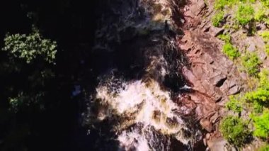 Top down view of fast river. Revealing the waterfall with swimming area and people on swimming pier at a camping site surrounded by a forest with pine trees. In Ambjorby Famtfallet Varmland Sweden