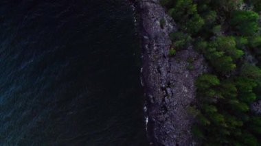 Evening top down view over the crashing waves against the rocky coastline of an island with pine trees, people walking on the rocks near the dark lake in Saffle Vanern lake Sweden. Nature scenery background in 4K resolution