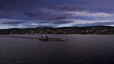 İnsanlar mavi saat günbatımında tahta iskelede ve göl kıyısında yürürler. İnsanlar yaz tatilinde şehrin güzel manzarasının, dağların ve mavi gökyüzünün dramatik bulutlarının tadını çıkarıyorlar. Siljan Gölü, Rattvik, Dalarna, İsveç Hava Görüntüsü 4K