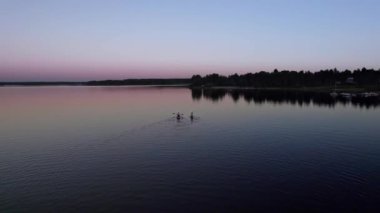 Havadan çekilen görüntüler, göldeki bir yemek masasında kürek çeken iki genç kadın, sağlık aktivitesi, su sporu. Sakin göl, Nas bruk, Dalarna İsveç 'te renkli bir yaz günbatımı ile çevrili.