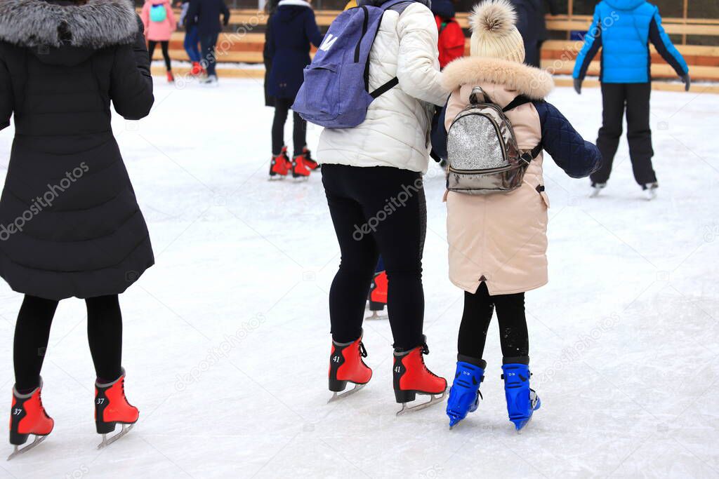 Little girl skates on a skating rink in winter. A woman teaches a child to skate. Sports clubs, active family sports for children, winter holidays, Christmas and New Year.