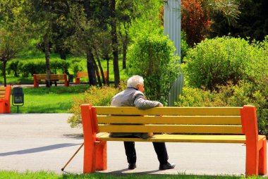 Bahar parkında bir bankta oturan yaşlı adam. Yaşlı emekli vatandaş güneşli yaz gününde ahşap bir bankta dinleniyor..