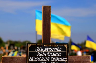 The grave of unknown soldier who died in war against, the background of flags Ukraine. A plate at cemetery with inscription in Ukrainian - temporarily unknown defender of Ukraine is buried here.