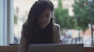Young Moroccan Girl With Curly Hair Wearing Glasses Using Laptop. Medium Shot - Horizontal