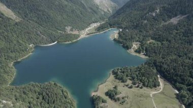 Fransa 'nın Pireneler kentindeki verimli yeşil bitki örtüsüyle çevrili Ayous Gölü üzerindeki hava görüntüsü güneşli bir sabahta çekilmiştir. - Yatay 4K videosu