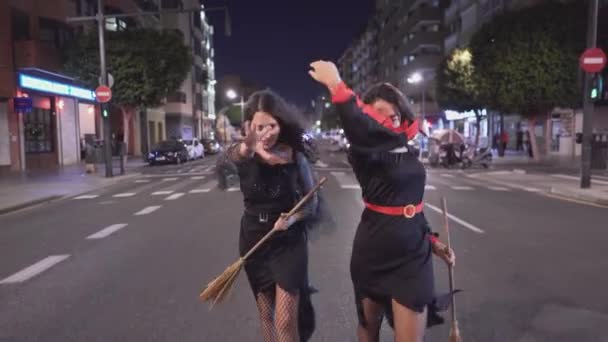 魔女の衣装を着た2人の美しいコロンビア人女性が歩き バレンシアでハロウィーンの休日の夜に街のカメラに向かって走り始めます スペイン プルバックショット — ストック動画
