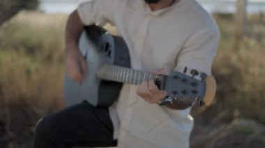 Kırsal kesimde gitar çalan İspanyol sakallı hippi. Geri çekil, ağır çekimde 4K video.