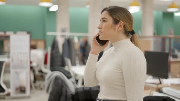 ビジネスマンの女性は携帯電話を使って会話をしている コワーキングスペースで携帯電話の音を聞きながら顔の表情を真剣にしている女 横顔4K動画 — ストック動画