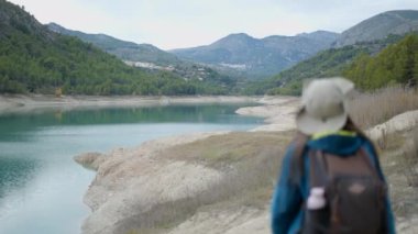 Young woman in trekking gear walks away from camera by lake in Spain - Horizontal video
