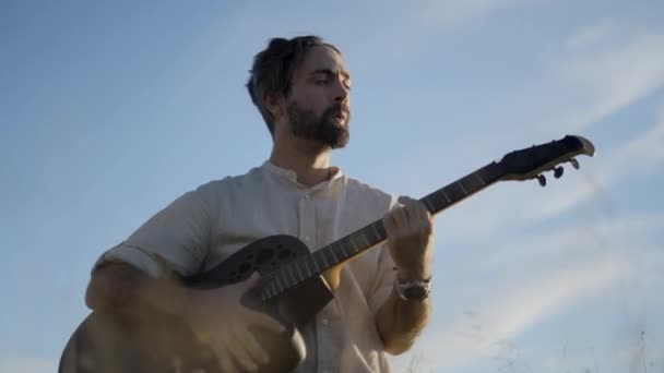 西班牙胡子大男子主义吉他手在蓝天背景下弹奏吉他和唱情歌 水平4K视频 — 图库视频影像