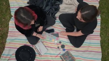 birds eye over two girls on black clothes sitting on a colored mat, chatting about cosmetics makeup - Horizontal 4K video