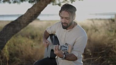 Serseri müzisyen yol kenarında akustik gitarla şarkı söylüyor ve çalıyor. Güneşin batışıyla aydınlanıyor. Yatay dönüm - 4K video