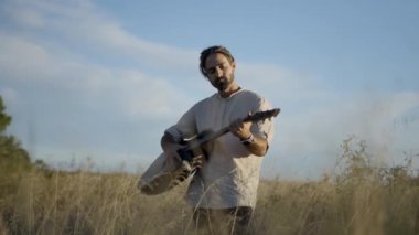Gitarda melodi çalan yakışıklı adam, İspanya 'nın sonbaharında sarı kurumuş çayırında dikilirken gökyüzü ağlar - 4K yatay video