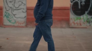 man dressed in jeans and sweater walking on sidewalk, lower body. slowmotion, tracking shot - Horizontal 4K video