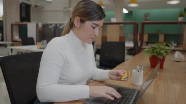 Ofisteki dizüstü bilgisayarda kredi kartı numarasıyla internetten alışveriş yapan kadın - 4K yatay video