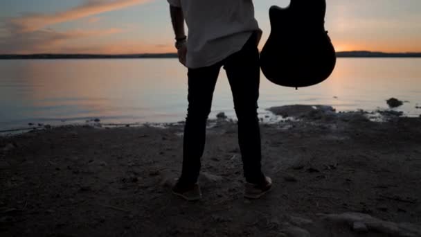 男子站在湖边 在灿烂的金色夕阳西下 将吉他举到空中 西班牙阿尔利坎特的Torrevieja Pink湖 向后看Gimbal起重机 水平4K视频 — 图库视频影像