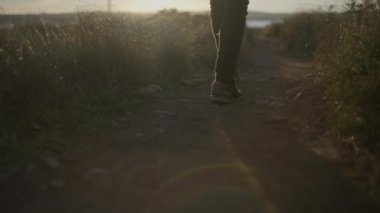 Gün batımında elinde gitarla kırsal bir yolda yürüyen adamın bacakları - yavaş çekim - yatay 4K video