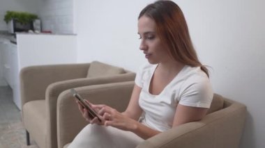 Young Lady In A Couch Browsing On Her Tablet At Home. Medium Shot - Horizontal