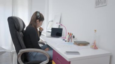 Evde okuyan genç Kolombiyalı kız öğrenci egzersiz kitabında özet notlar okuyor bilgisayarla online öz eğitim yapıyor masa başı araştırma ödevi yapıyor. -