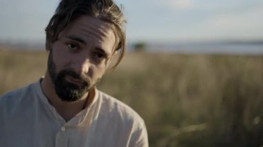 Gün batımında gitar çalan ve nehir kenarında şarkı söyleyen sakallı İspanyol adam - yüz yüze - yatay 4K video