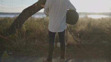 Akustik gitar çalan çekici beyaz adam, İspanya 'nın yol kenarında dikilirken günbatımı ışıklarıyla aydınlanıyor.