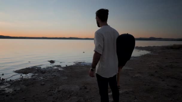 スペインのアリカンテにあるTorreevieja Pink湖のそばに立つ夕日を楽しむギターを持つ男 横4K動画 — ストック動画