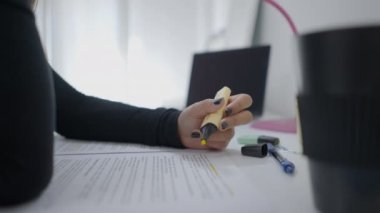 Close up shot of an unrecognizable young girl sitting at a desk and highlighting some documents. Universitary student studying at home. - 4K Horizontal video