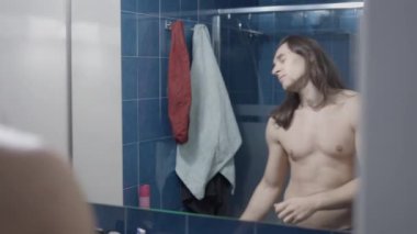 Banyodaki aynanın önünde dans eden uzun saçlı adam yavaş çekim, yatay video.