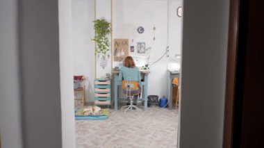 Stüdyoda çalışan bir kuyumcunun arka görüntüsü. Yerlerde yatan evcil bir köpek. Dolly 4K Yatay Görüntü