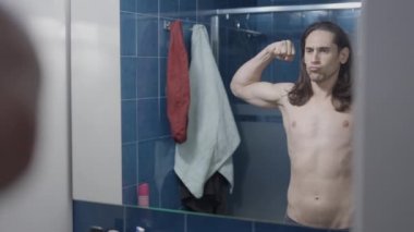 Genç çıplak adam banyo aynasının önünde kaslarına bakıyor - orta çekim - yatay video