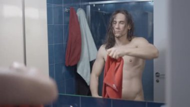 Genç metroseksüel adam banyodaki aynanın önünde saçını kurutuyor kırmızı havluyla duş aldıktan sonra - orta çekim - yatay video