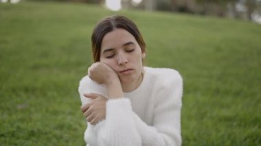 Young exhausted woman sits on grass resting head on hands, shut eyes - 4K Horizontal video