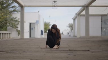 Young woman dressed in black sits on wooden bridge and looks down - 4K Horizontal video