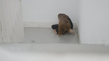 Young woman sits in corner of stairwell and moves with hair in face - 4K Horizontal video