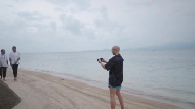 Photographer take pictures of a gay couple walking together by the sea during their honeymoon - 4K Horizontal video