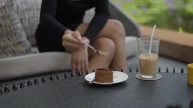 Kanepede oturan Asyalı bir kız restoranda bir dilim kek yiyor. 4K yatay video.